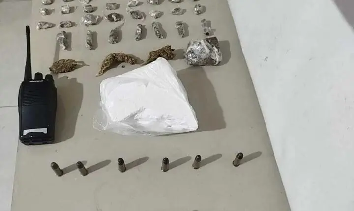 Ao abrir portão de casa denunciada por tráfico, jovem se depara com a PM, tenta impedir entrada e acaba preso com drogas, arma e munições